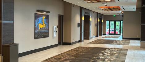 A modern hotel corridor with a large painting, multiple doors, and a patterned carpet.