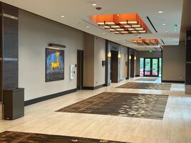 Un pasillo moderno de hotel con un cuadro grande, varias puertas y una alfombra estampada.