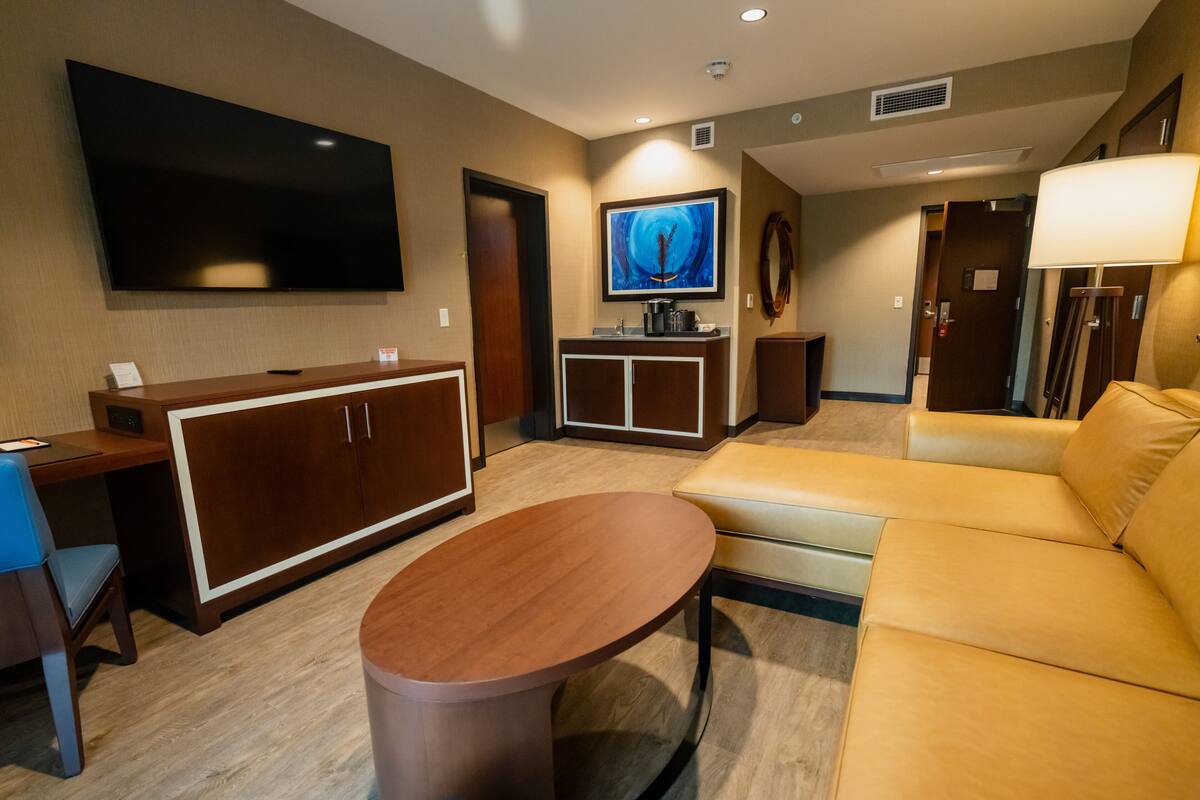 A hotel room with a flat-screen TV, a wooden desk, a sofa, and a coffee table.