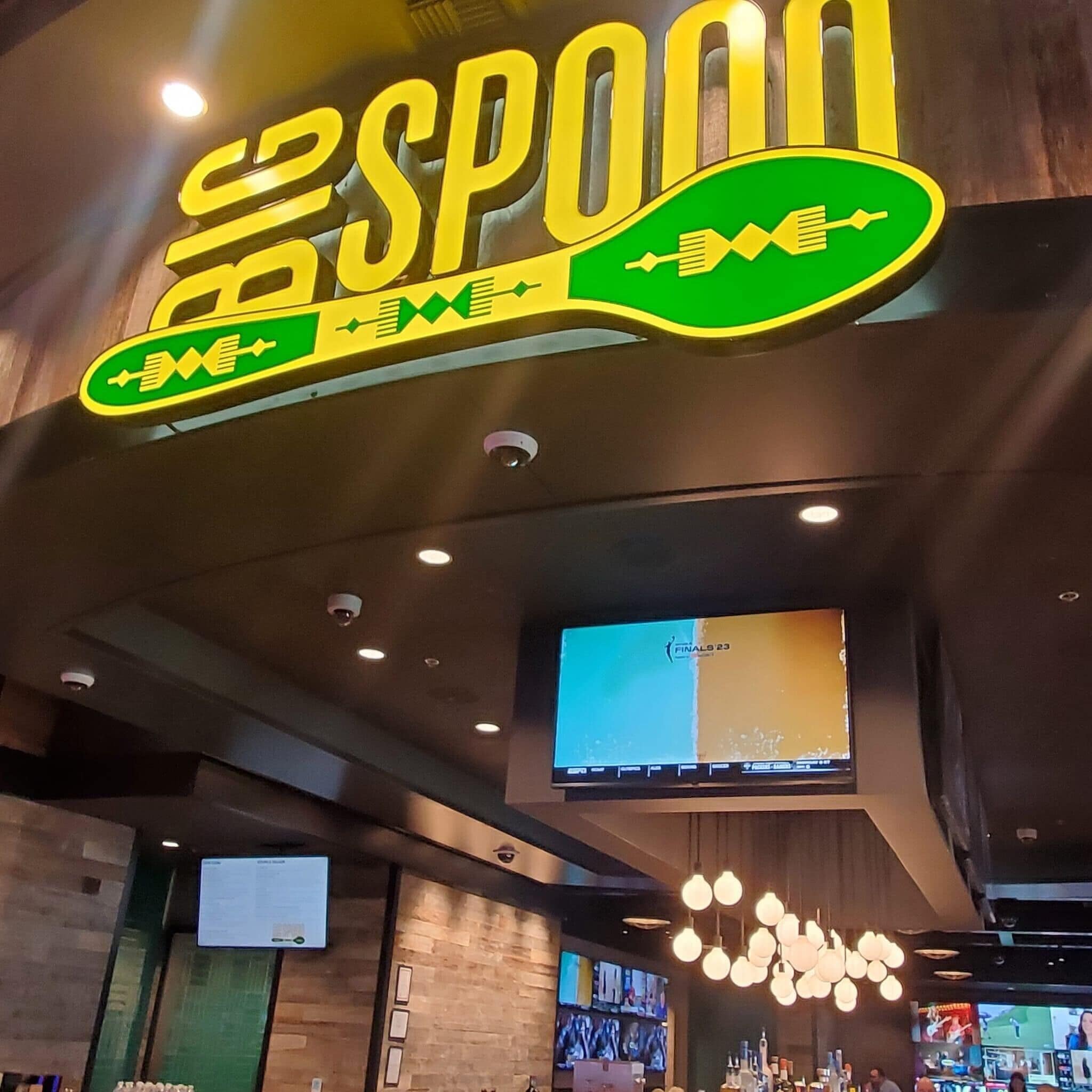 A bar area with a large neon sign reading "SPON", a television screen, and hanging spherical light fixtures.