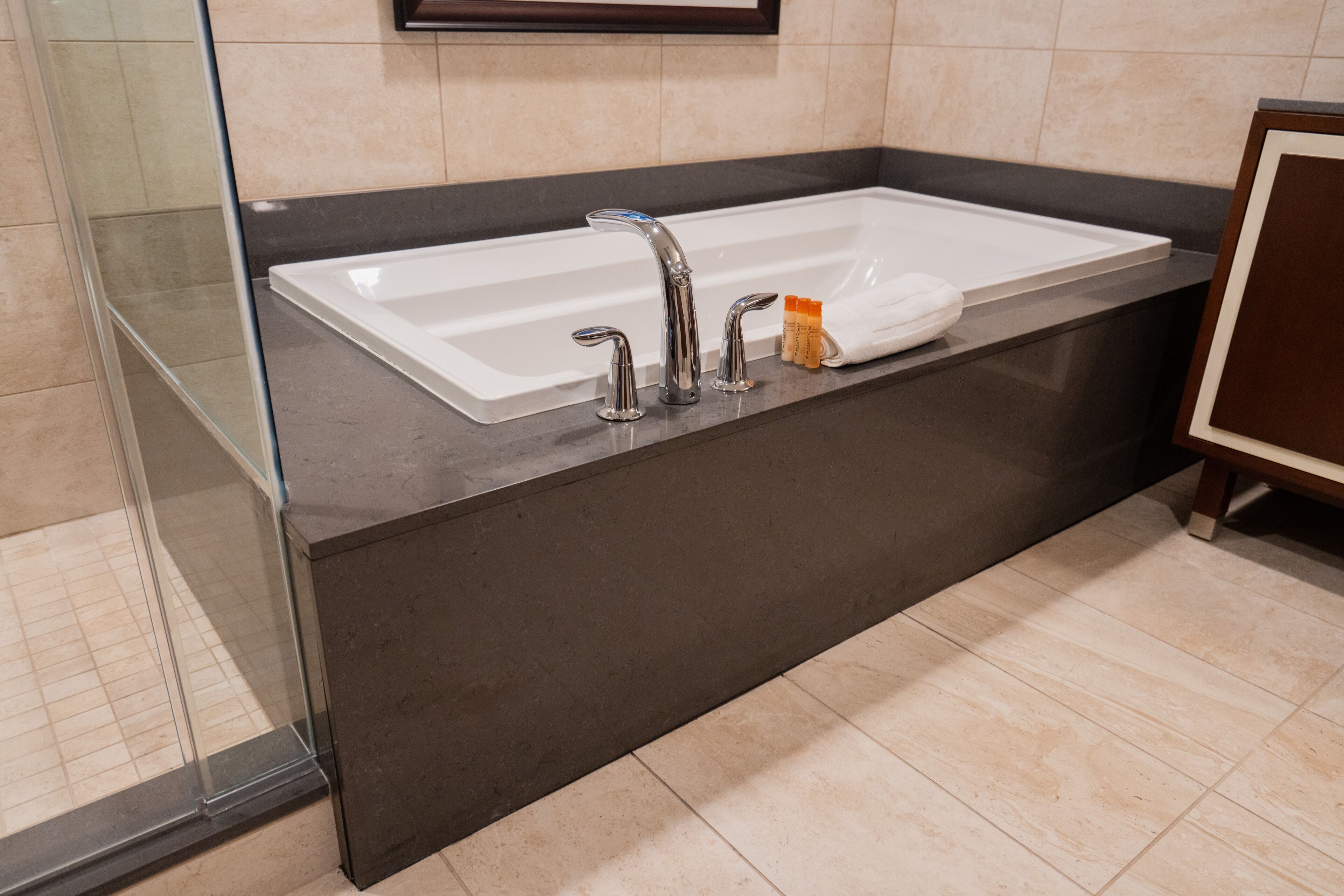 A modern bathroom with a large white sink, two faucets, and a glass shower enclosure.