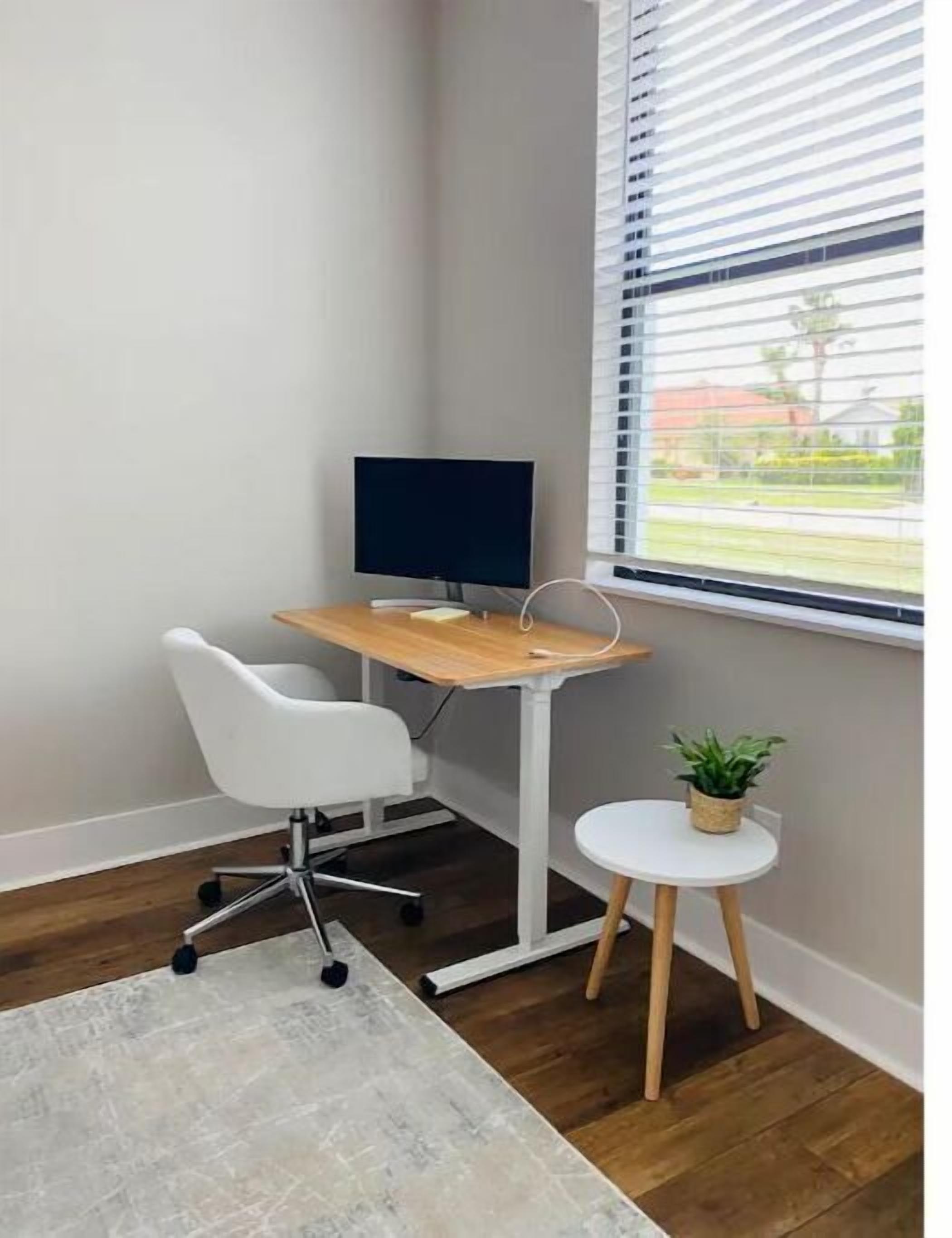 Ein Büro im Eck mit Schreibtisch, Stuhl und einem kleinen Tisch mit Pflanze.