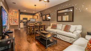 A modern living room with a sofa, coffee table, and TV. There's a kitchen in the background with cabinets and a microwave. - Spacious 3BR Townhome in Kissimmee, perfect for family getaways! (Kissimmee)