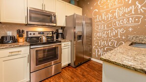 A modern kitchen with stainless steel appliances, white cabinetry, and a decorative wall with inspirational text. - Spacious 3BR Townhome in Kissimmee, perfect for family getaways! (Kissimmee)