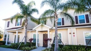 A two-story residential building with a front porch, palm trees, and a well-maintained lawn. - Spacious 3BR Townhome in Kissimmee, perfect for family getaways! (Kissimmee)