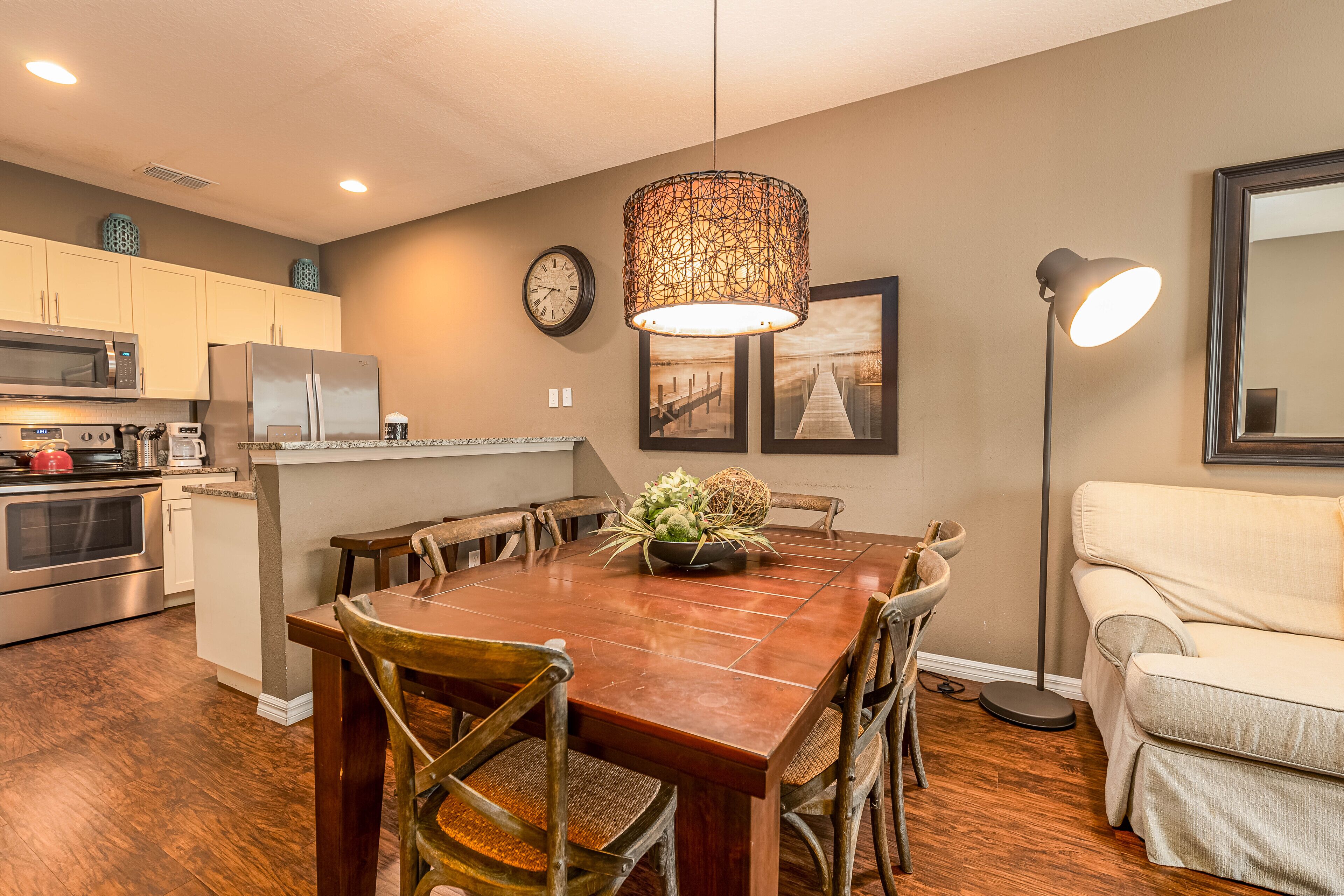 A modern kitchen with a dining area, featuring a wooden table, chairs, a hanging light fixture, and a refrigerator.