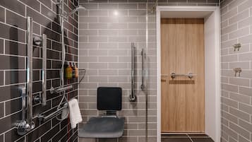 A modern bathroom with grey tiles, a wooden door, a shower area, and a toilet with a towel rack.