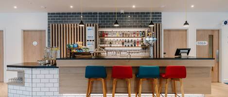 A modern bar area with a counter, stools, and a variety of bottles.
