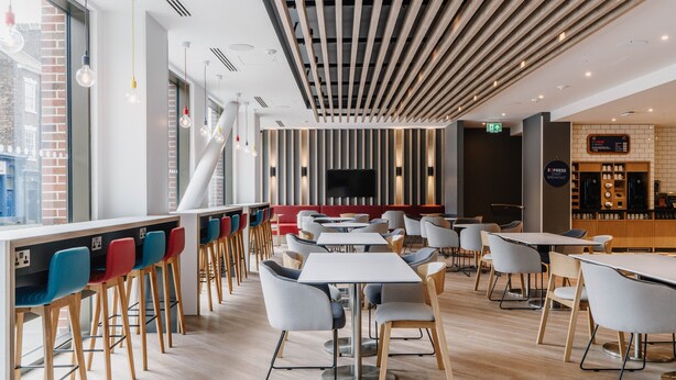 A modern restaurant with high tables and chairs, a bar area, and a large TV screen. - Holiday Inn Express Liverpool Central by IHG (Liverpool)