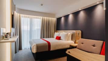 A hotel room with a bed, bedside table, and a seating area.