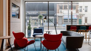 A modern interior with red and grey chairs, a round table, and a view of the Liverpool Branch Place building. - Holiday Inn Express Liverpool Central by IHG (Liverpool)