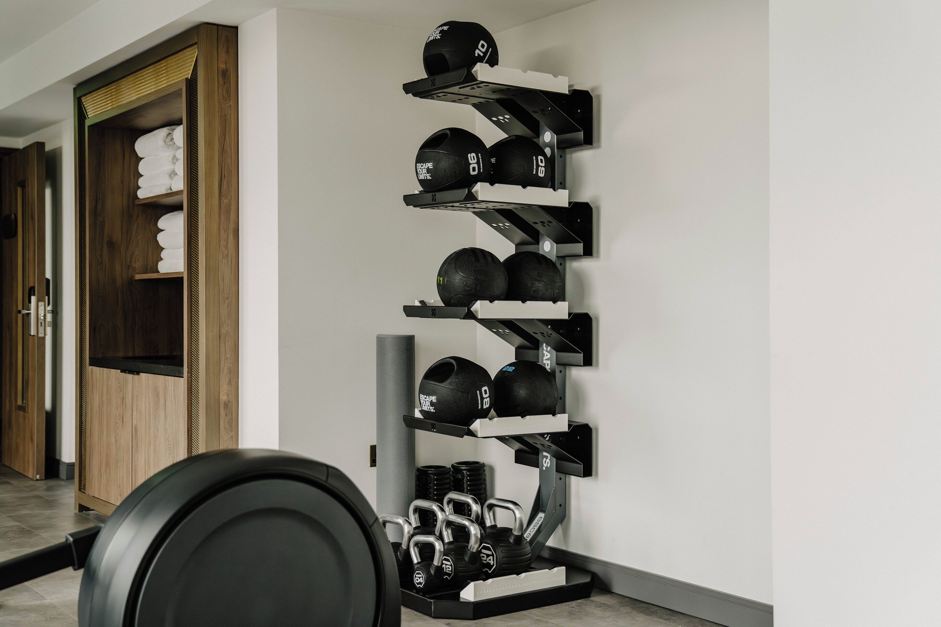 A gym with a wall-mounted rack holding various exercise balls and dumbbells.