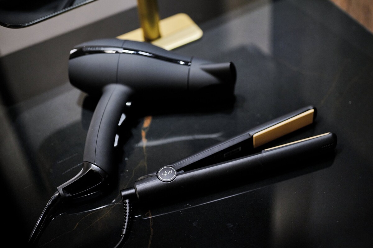 A black hairdryer and a flat iron on a black countertop.
