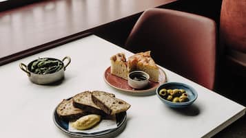 Una mesa con una fuente de pan, un cuenco de aceitunas y un bol de verduras.