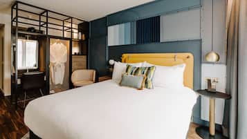 A modern hotel room with a large bed, a desk, a chair, and a wardrobe.