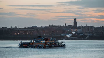 Een rivierboot met een kleurrijk ontwerp, en op de achtergrond een stadszicht met gebouwen en een klokkentoren.
