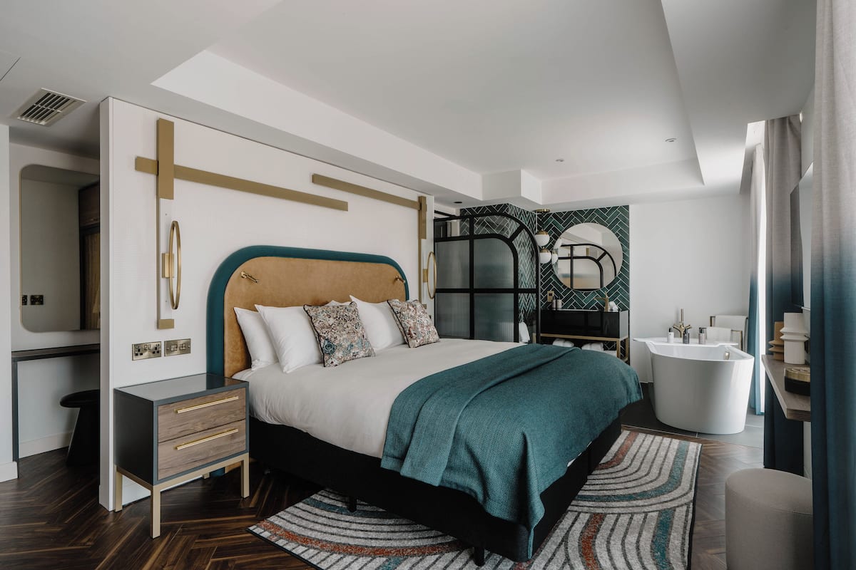A modern bedroom with a large bed, bedside tables, a built-in bathtub, and a mirror.