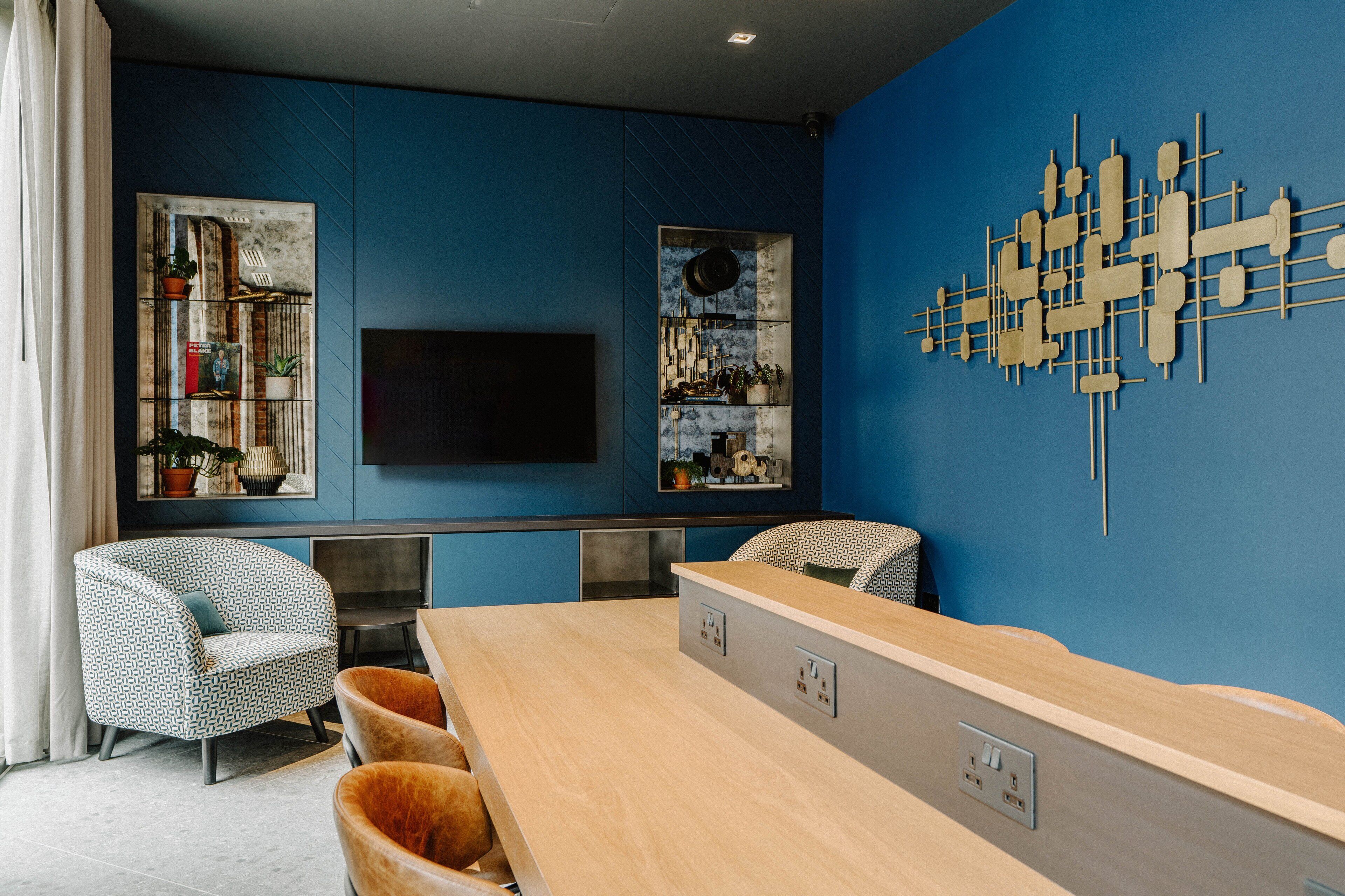 A modern living room with a blue accent wall, a flat-screen TV, a wooden coffee table, and patterned chairs.