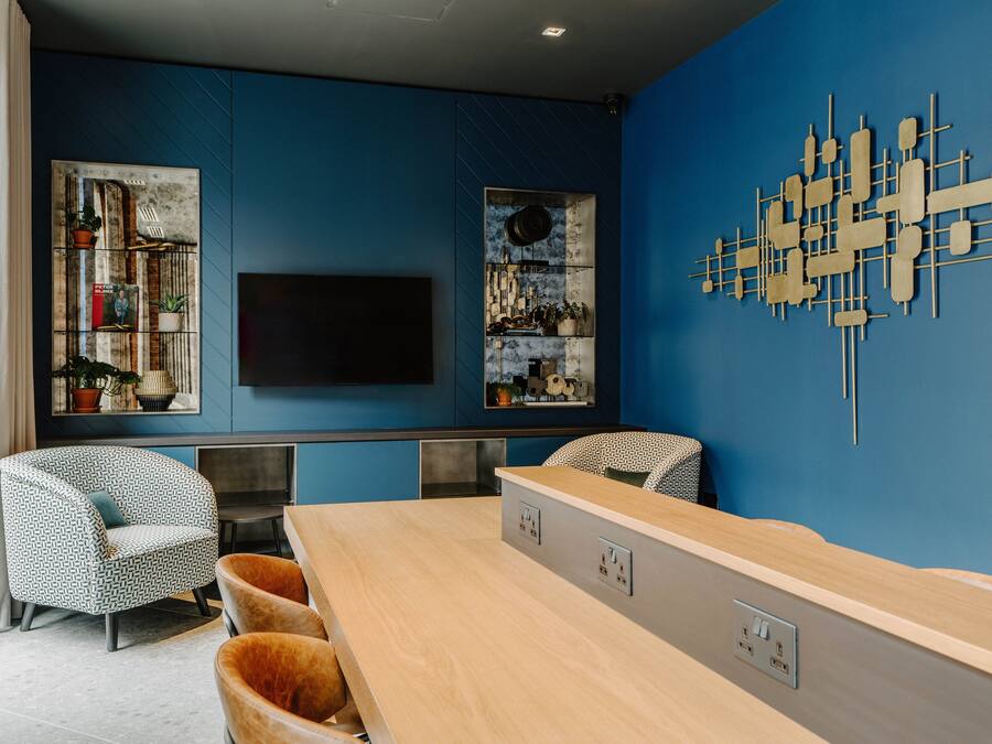 A modern living room with a blue accent wall, a flat-screen TV, a wooden coffee table, and patterned chairs.