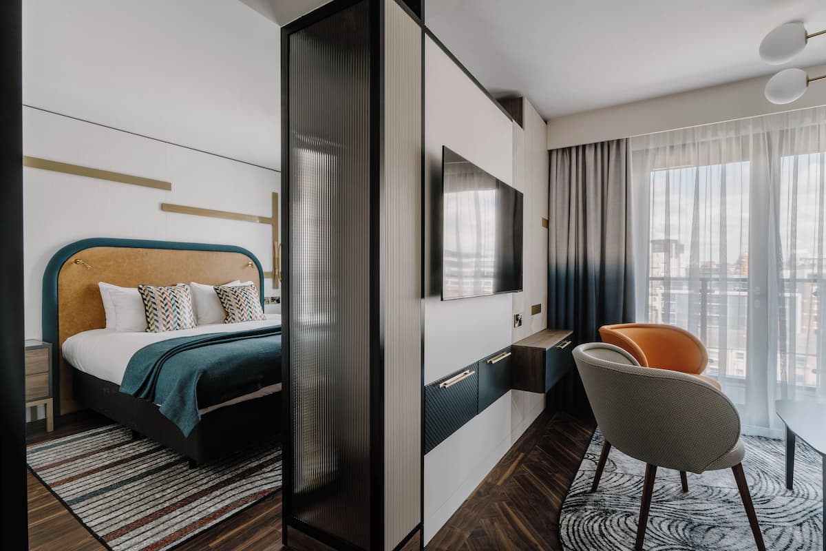 A modern hotel room with a bed, a desk, a chair, and a large window with a city view.