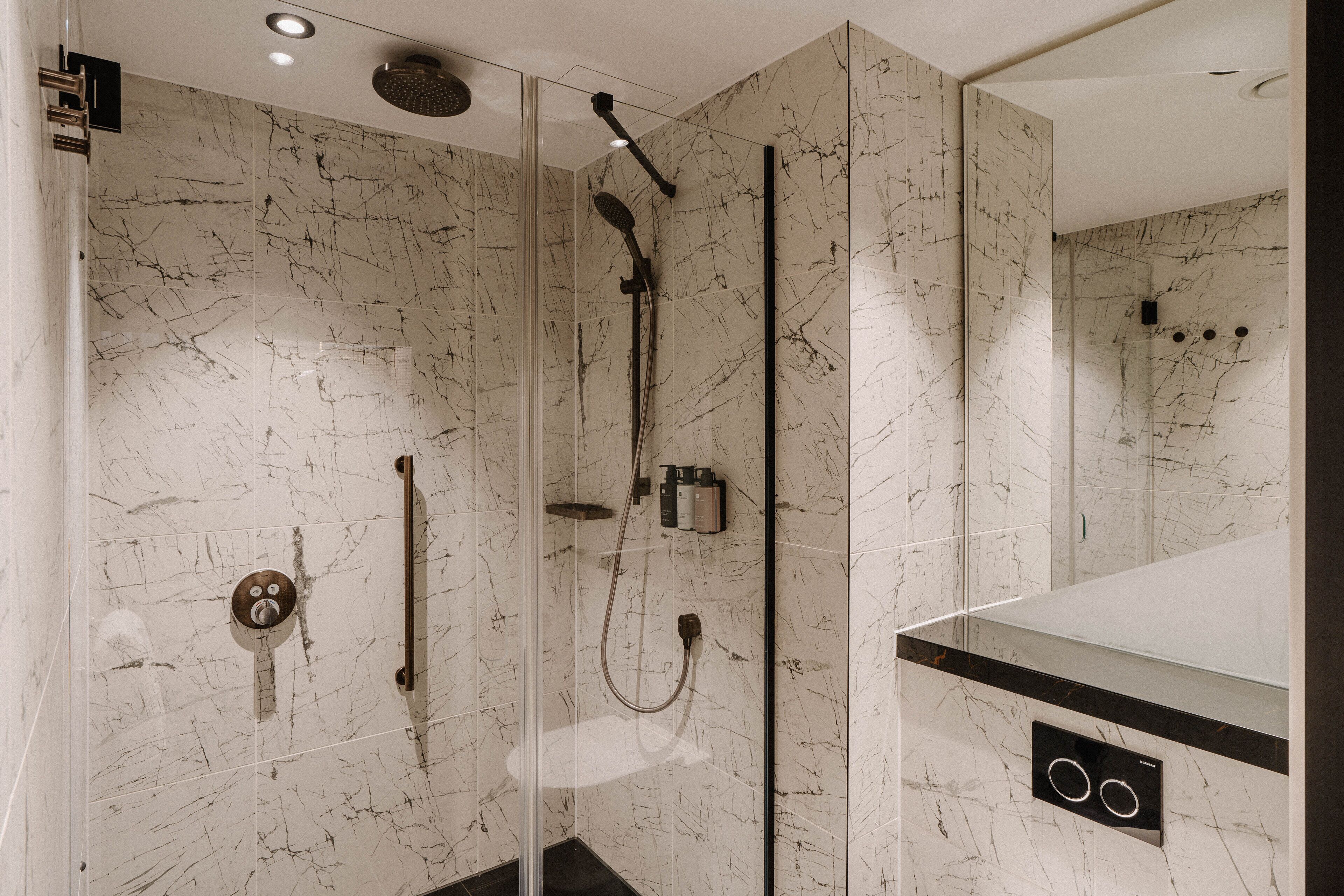 Un baño moderno con ducha de vidrio, paredes de mármol y encimera negra.