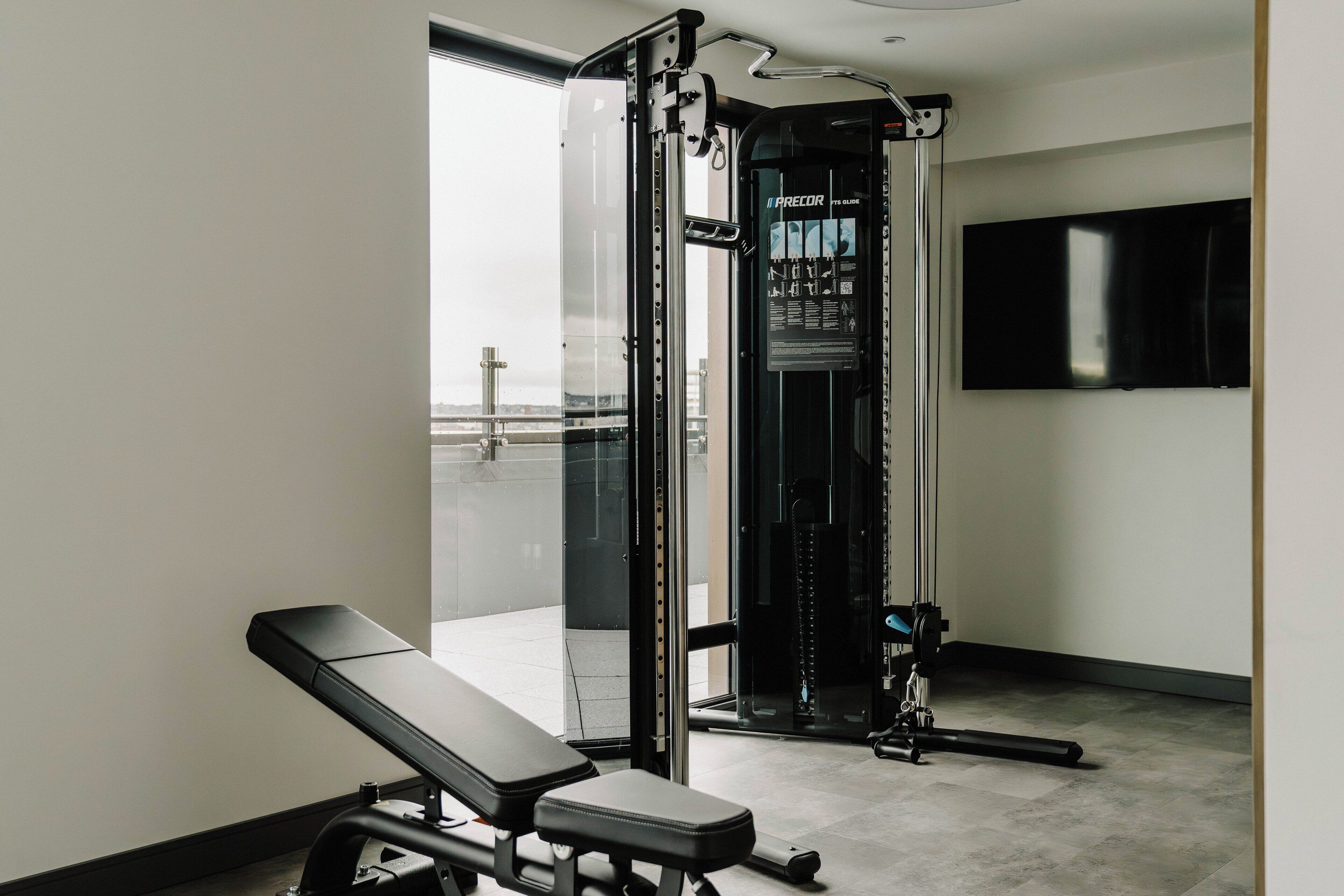 Une salle de sport équipée d’un banc, d’une machine de musculation et d’un téléviseur fixé au mur.