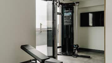 Une salle de sport équipée d’un banc, d’une machine de musculation et d’un téléviseur fixé au mur.
