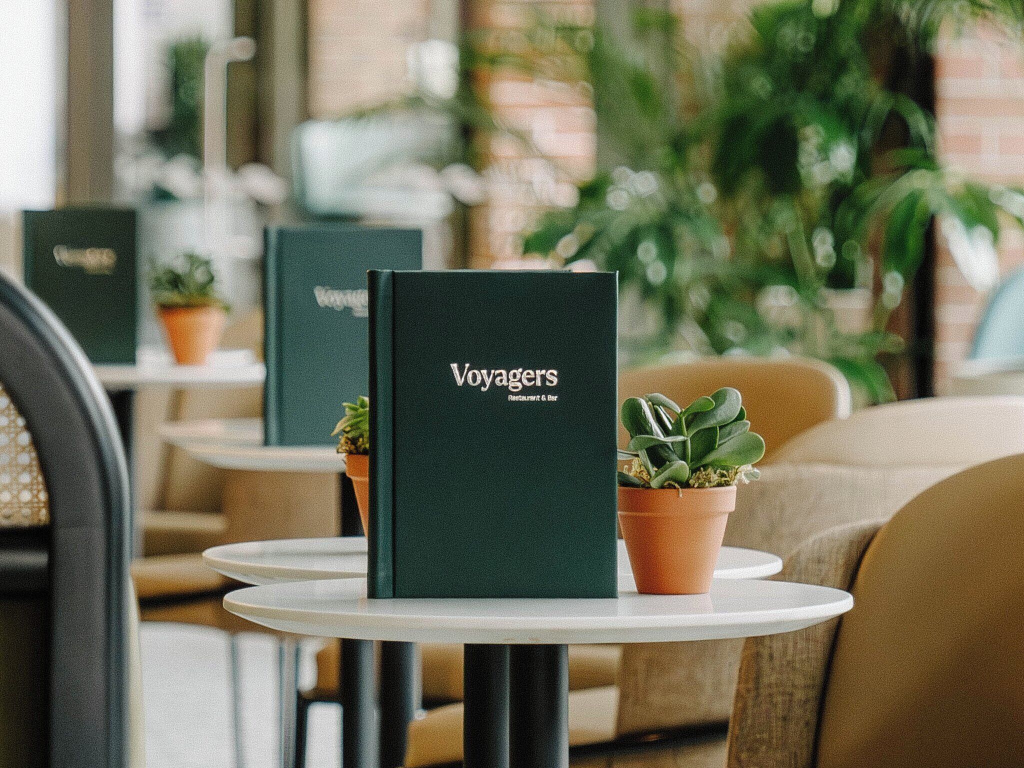 A menu stand with the word "Voyagers" on it, placed on a white table in a cafe setting.