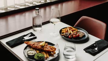 Una mesa de comedor con comida que incluye pescado con papas fritas, una botella de agua, una copa de vino y un plato de papas fritas con tomates y una rebanada de pan.