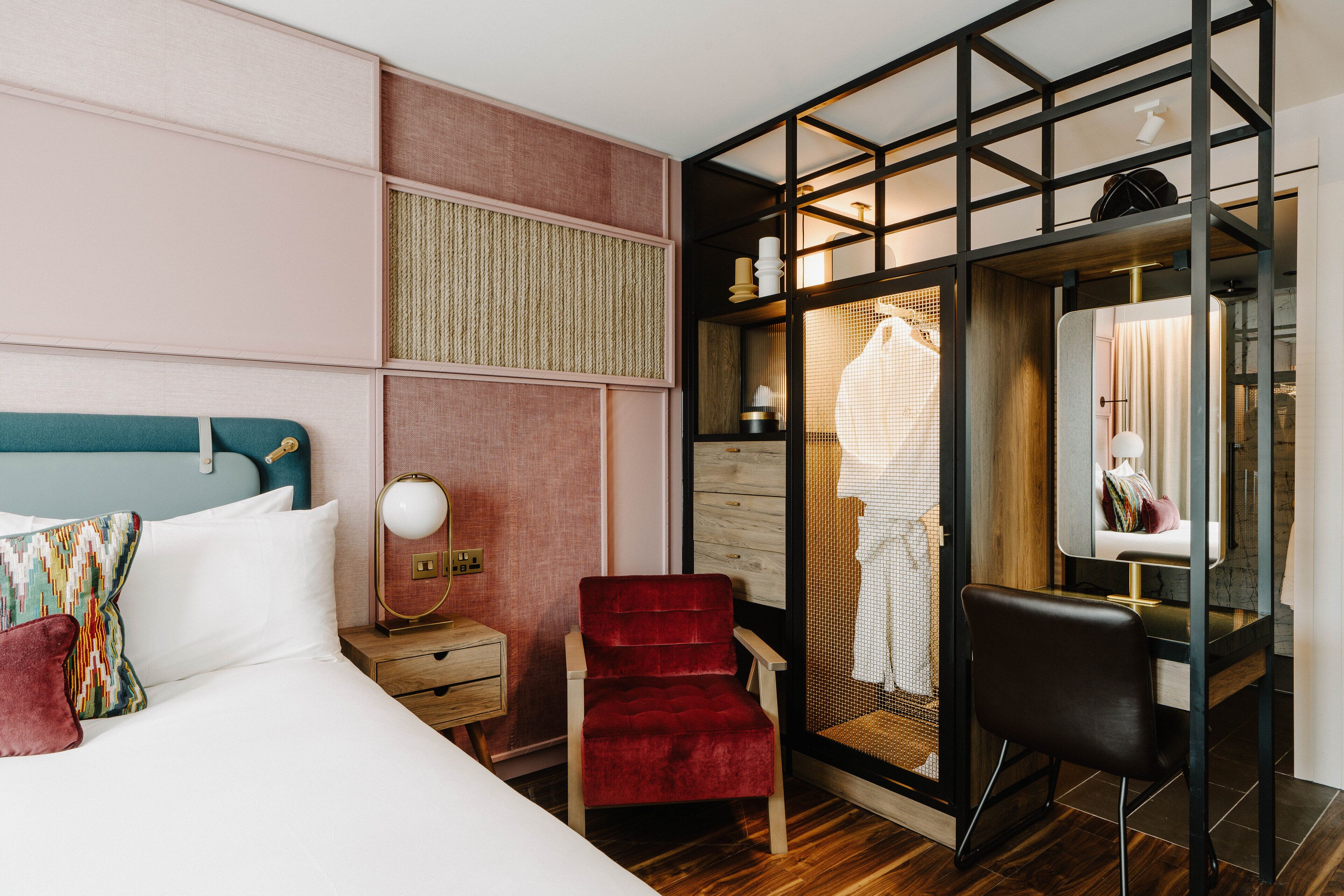 A hotel room with a bed, a red chair, a desk, and a wardrobe with a mirror.