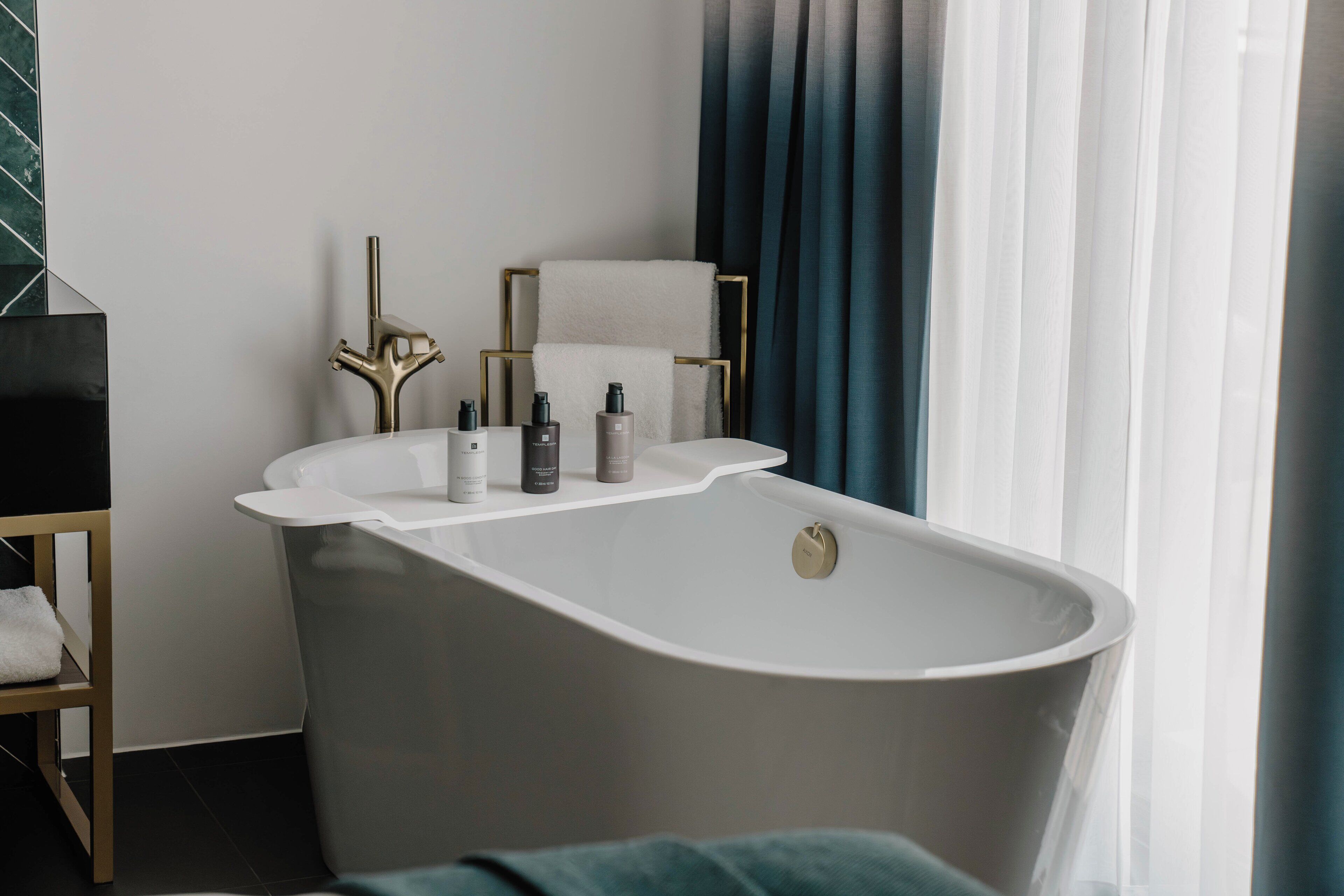 A modern bathroom with a freestanding bathtub, a towel rack, and a shelf with toiletries.