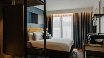 Una habitación de hotel moderna con una cama grande, un escritorio con lámpara y vistas a la ciudad a través de amplios ventanales.