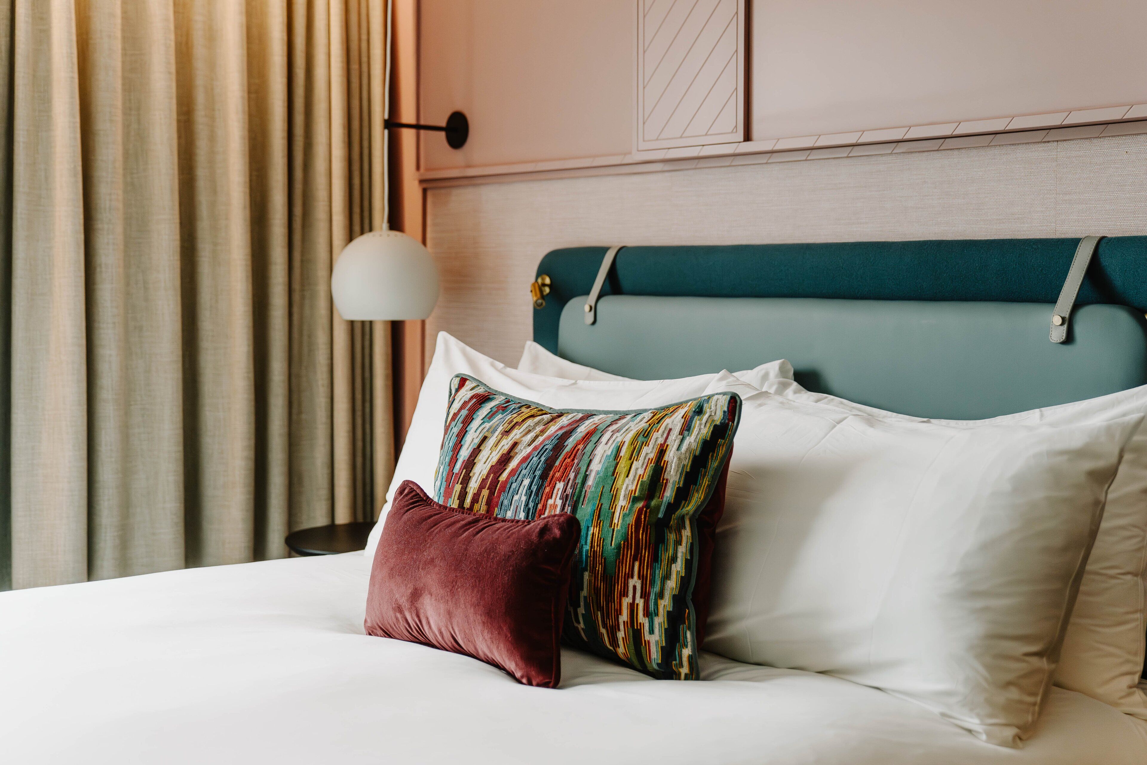 A bed with white and teal bedding, a colorful striped pillow, and a red pillow.