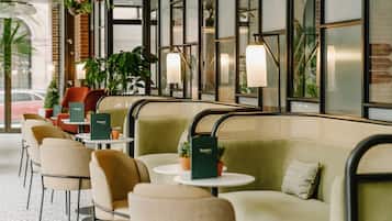 A cafe with cushioned seating, small round tables, and hanging plants.