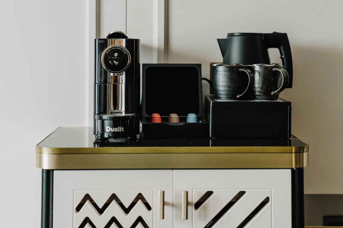 A coffee station with a coffee maker, a kettle, and a stack of mugs on a counter.