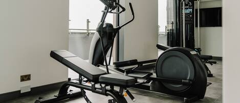 A gym with exercise equipment including a bench, elliptical, and stationary bike.