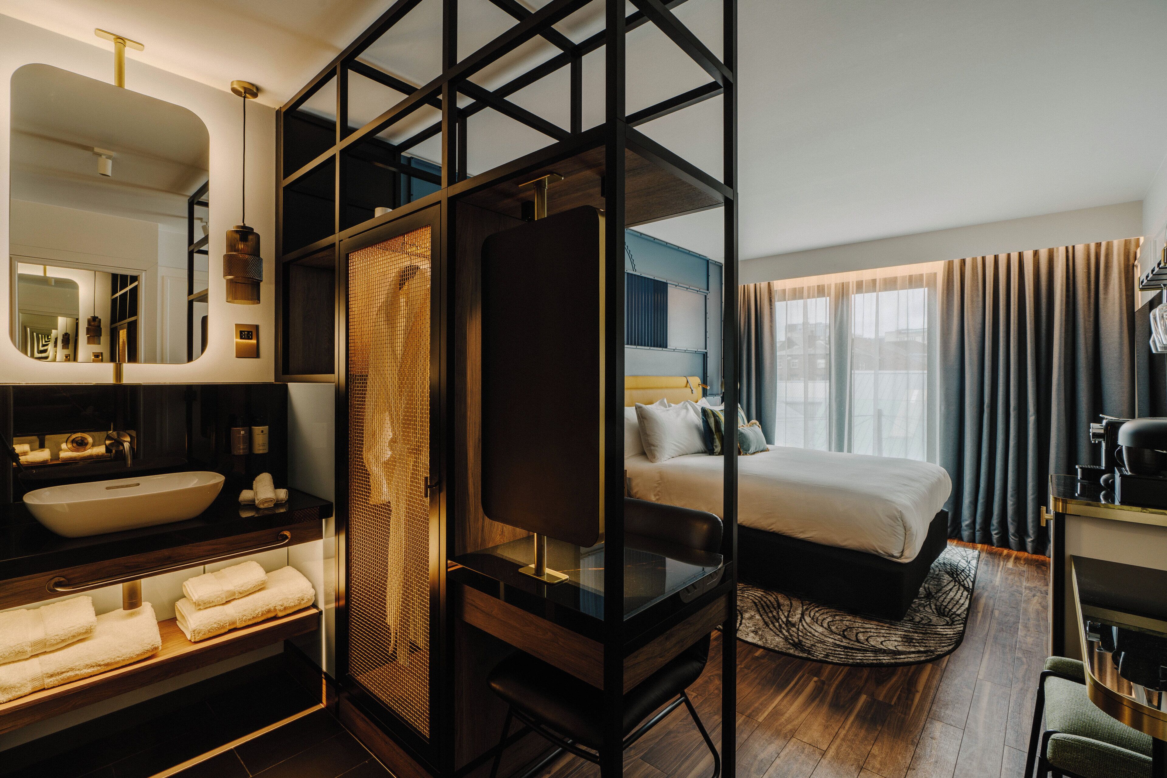 Habitación de hotel moderna con una cama grande, un área de baño separada, un espacio para sentarse y vistas a la ciudad por la ventana.