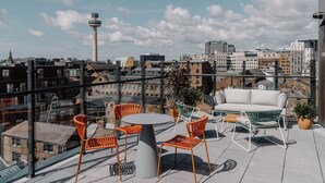 A rooftop terrace with a round table and orange chairs, overlooking a cityscape with historic buildings and a tower. - The Halyard Liverpool, Vignette Collection by IHG (Liverpool)