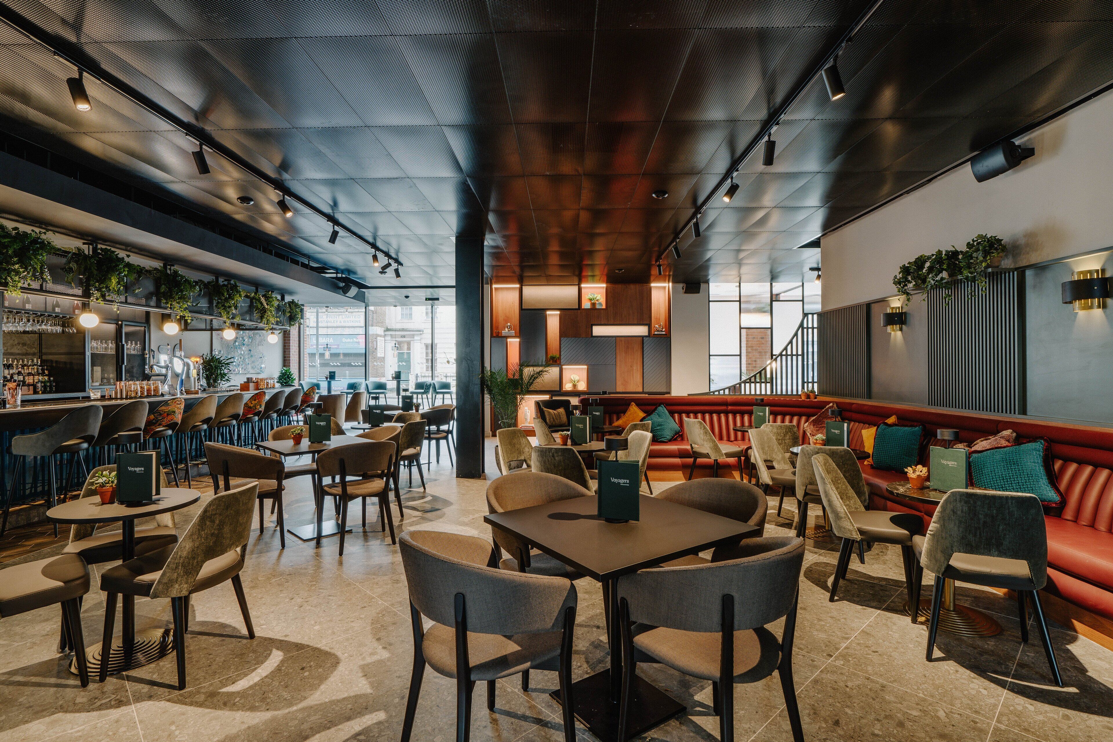 A modern restaurant with a bar area, seating with tables and chairs, and a red sofa.