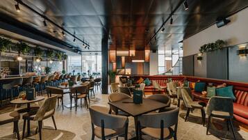 Um restaurante moderno com área de bar, mesas e cadeiras e um sofá vermelho.