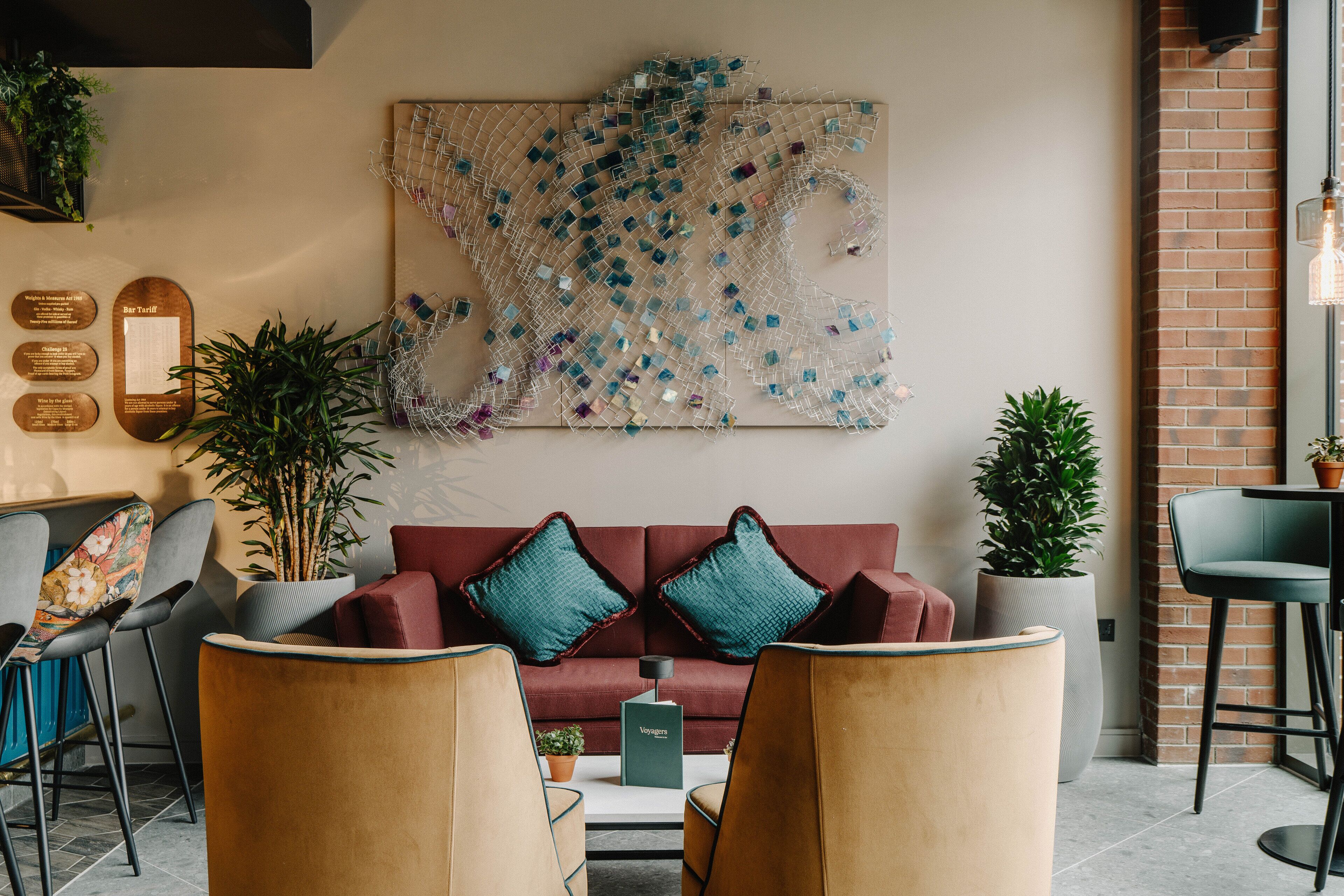 A modern lounge area with a red sofa, two armchairs, and a coffee table. There is a large abstract art piece on the wall and a potted plant on the right.