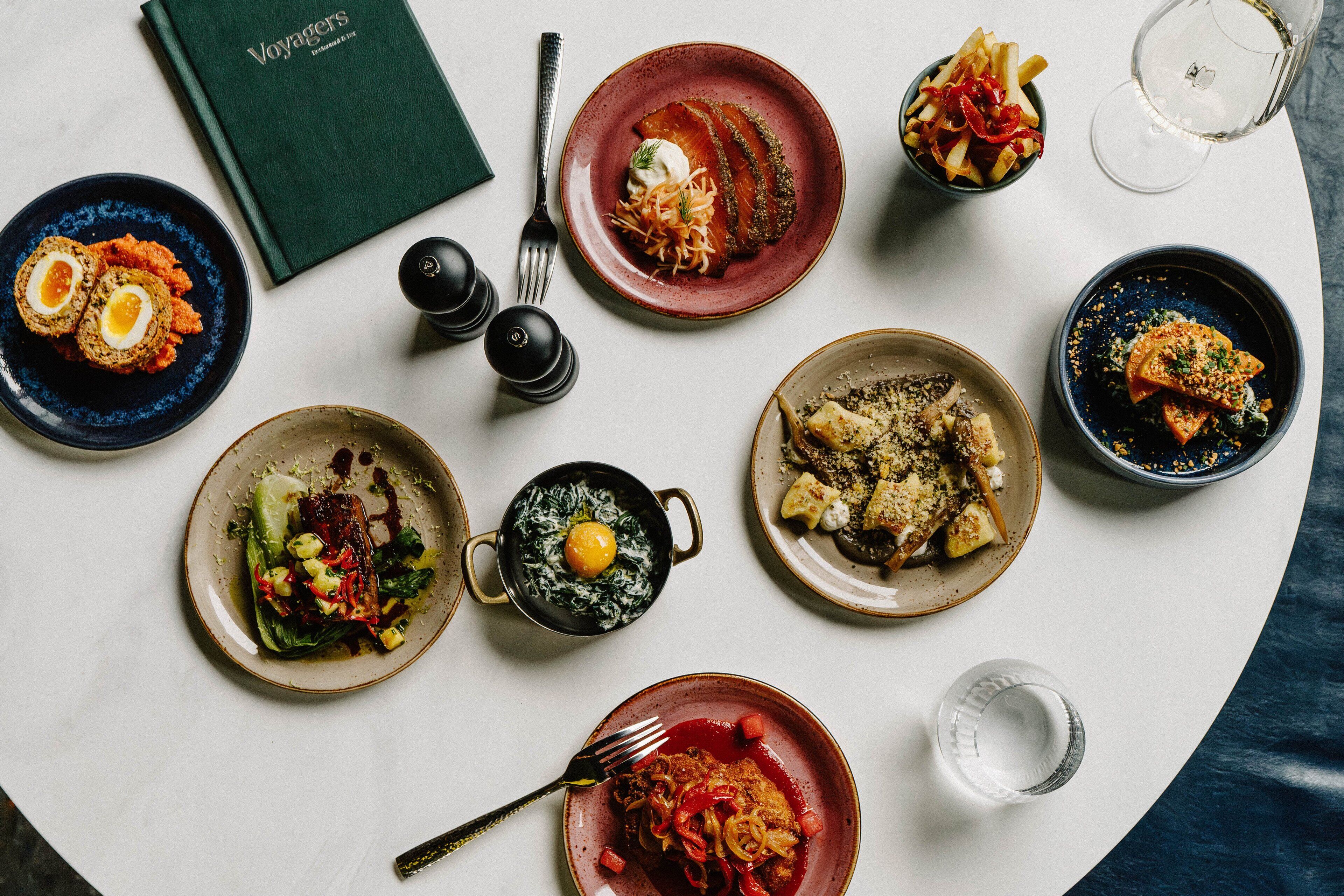 A table with various dishes, a book titled 'Voyagers', salt and pepper shakers, and a wine glass.