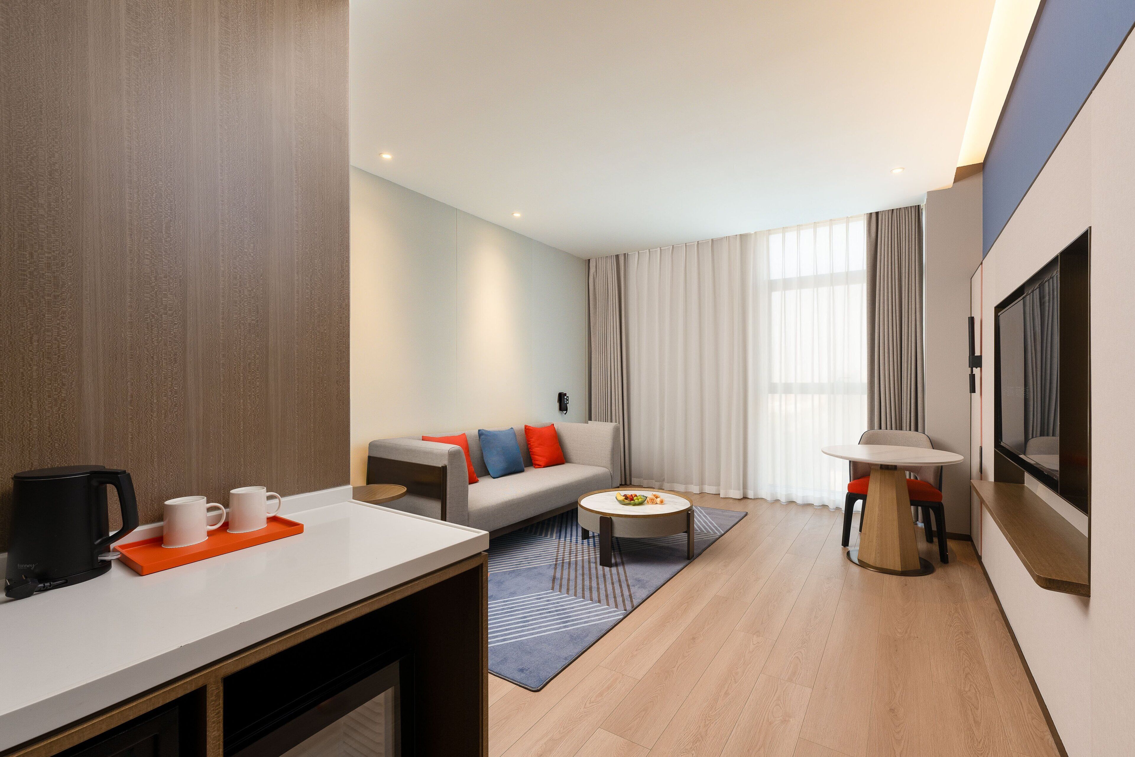 A modern hotel room with a sofa, coffee table, and a TV mounted on the wall.