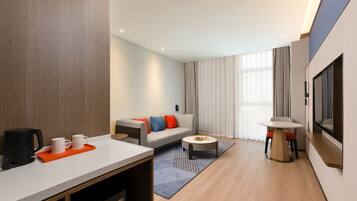 A modern hotel room with a sofa, coffee table, and a TV mounted on the wall.