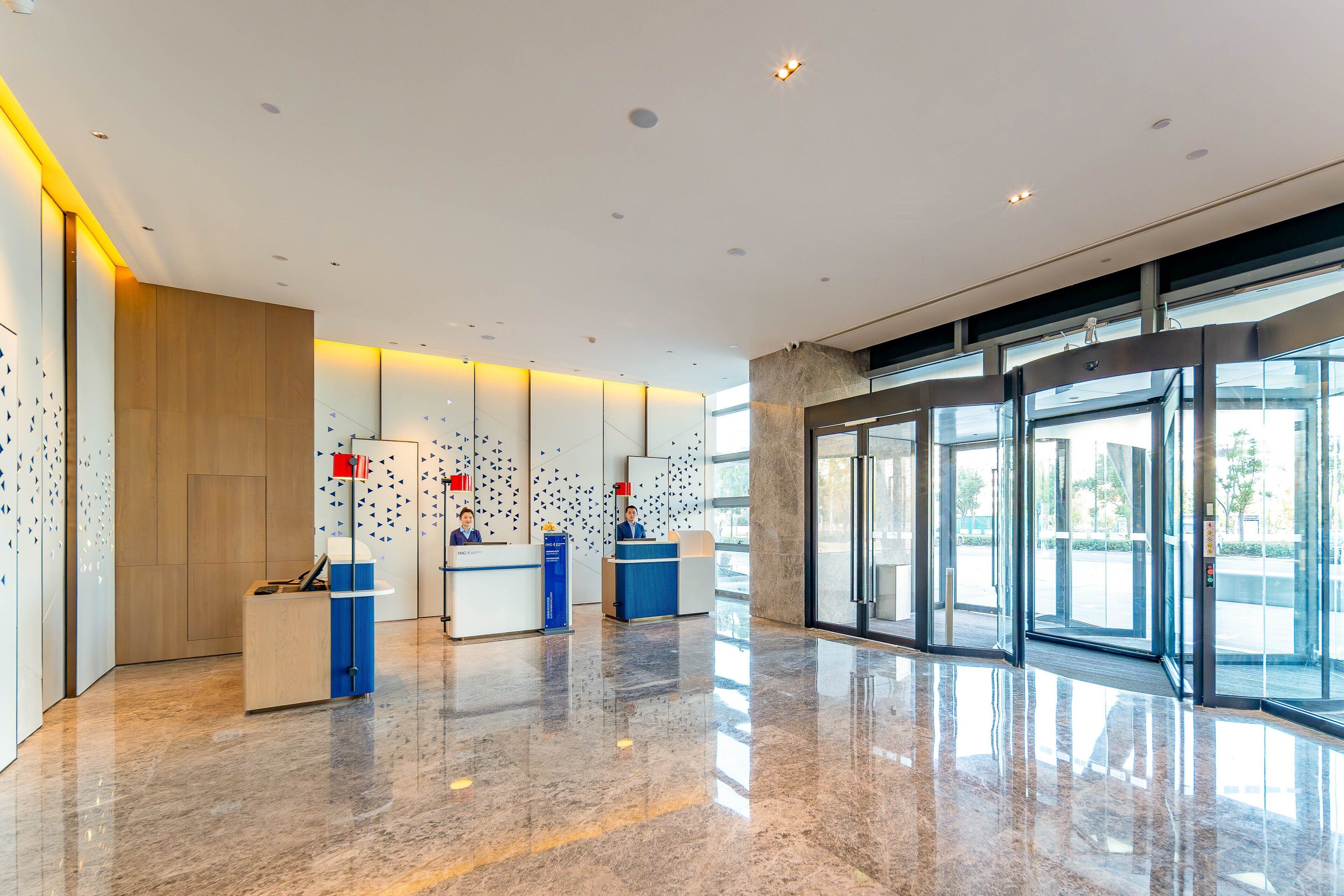 A modern reception area with a marble floor, glass doors leading outside, and a reception desk with a blue counter.