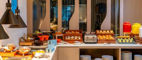 Disposição de buffet com diversos alimentos e utensílios, incluindo tigelas, pratos e bandejas de servir.