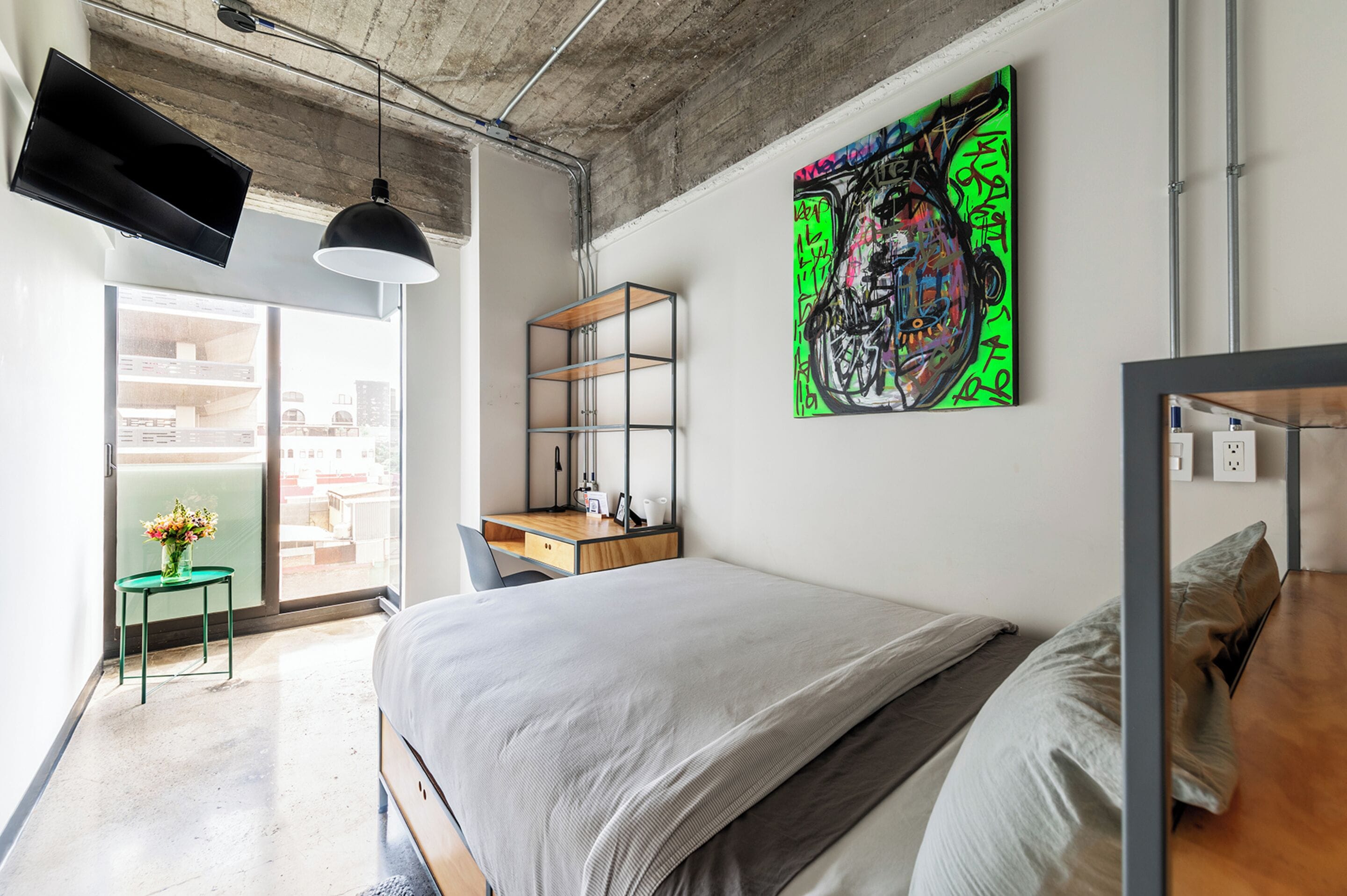 Ein modernes Schlafzimmer mit einem großen Bett, einem Schreibtisch und einem farbenfrohen Graffiti-Kunstwerk an der Wand.