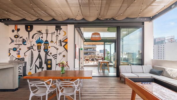 A modern interior with a wooden dining table, white chairs, a sofa, and a mural on the wall. - Triver Florencia (Mexico City)