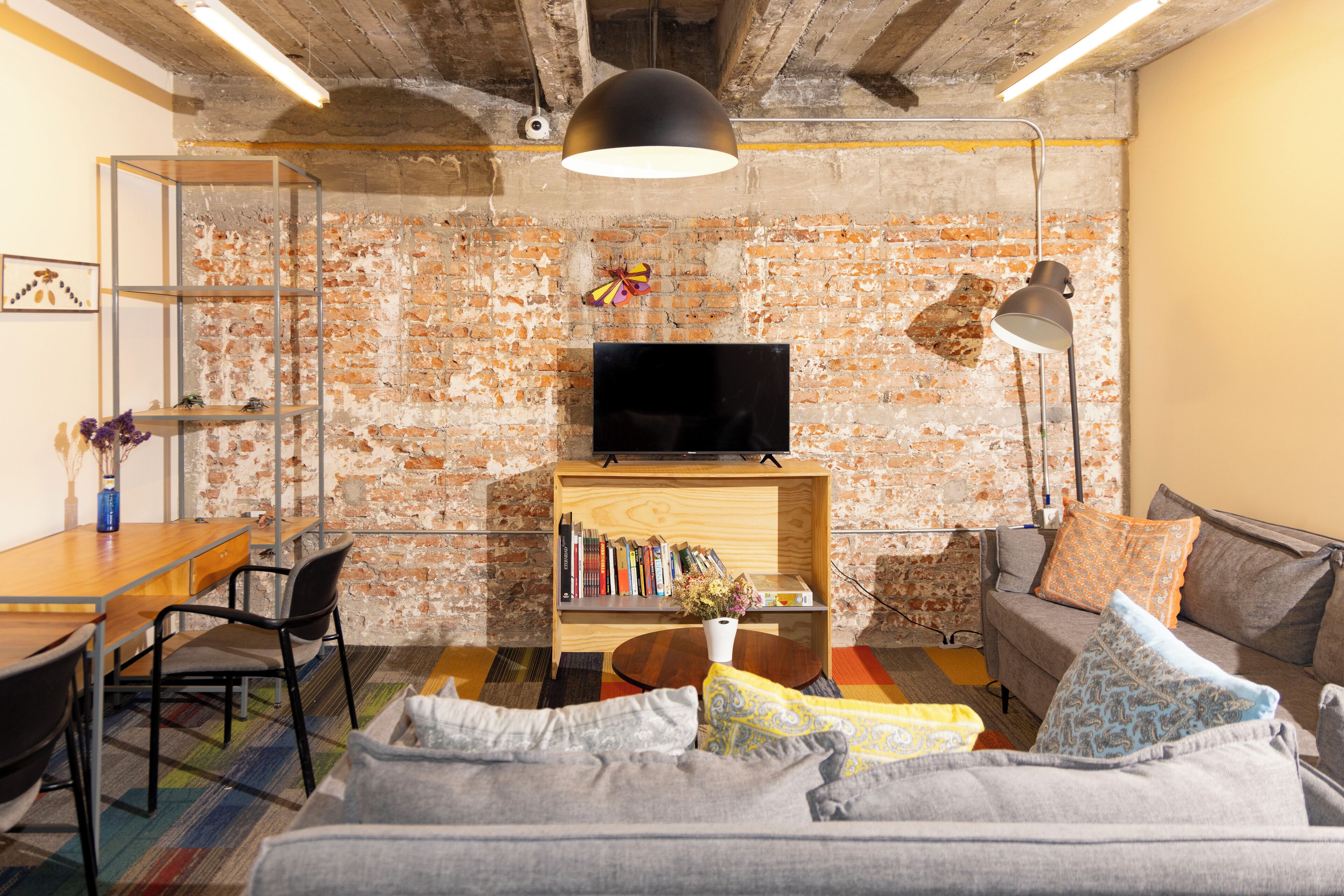 Una sala de estar con pared de ladrillo, un televisor sobre una estantería de madera, un sofá, una mesa de centro y un comedor con sillas y una mesa.