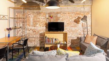 Una sala de estar con pared de ladrillo, un televisor sobre una estantería de madera, un sofá, una mesa de centro y un comedor con sillas y una mesa.